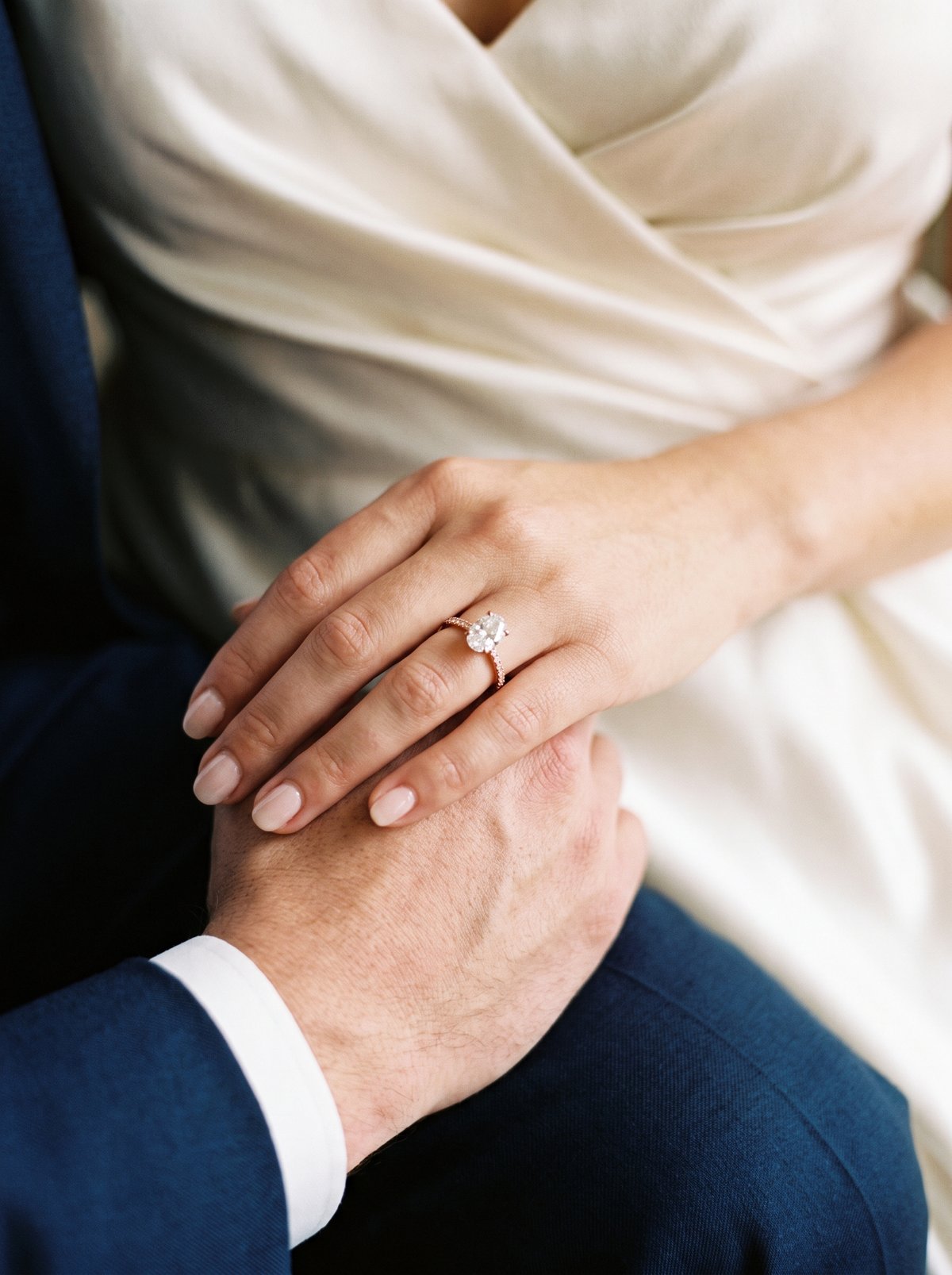 Two hands resting together, an oval diamond ring on her finger