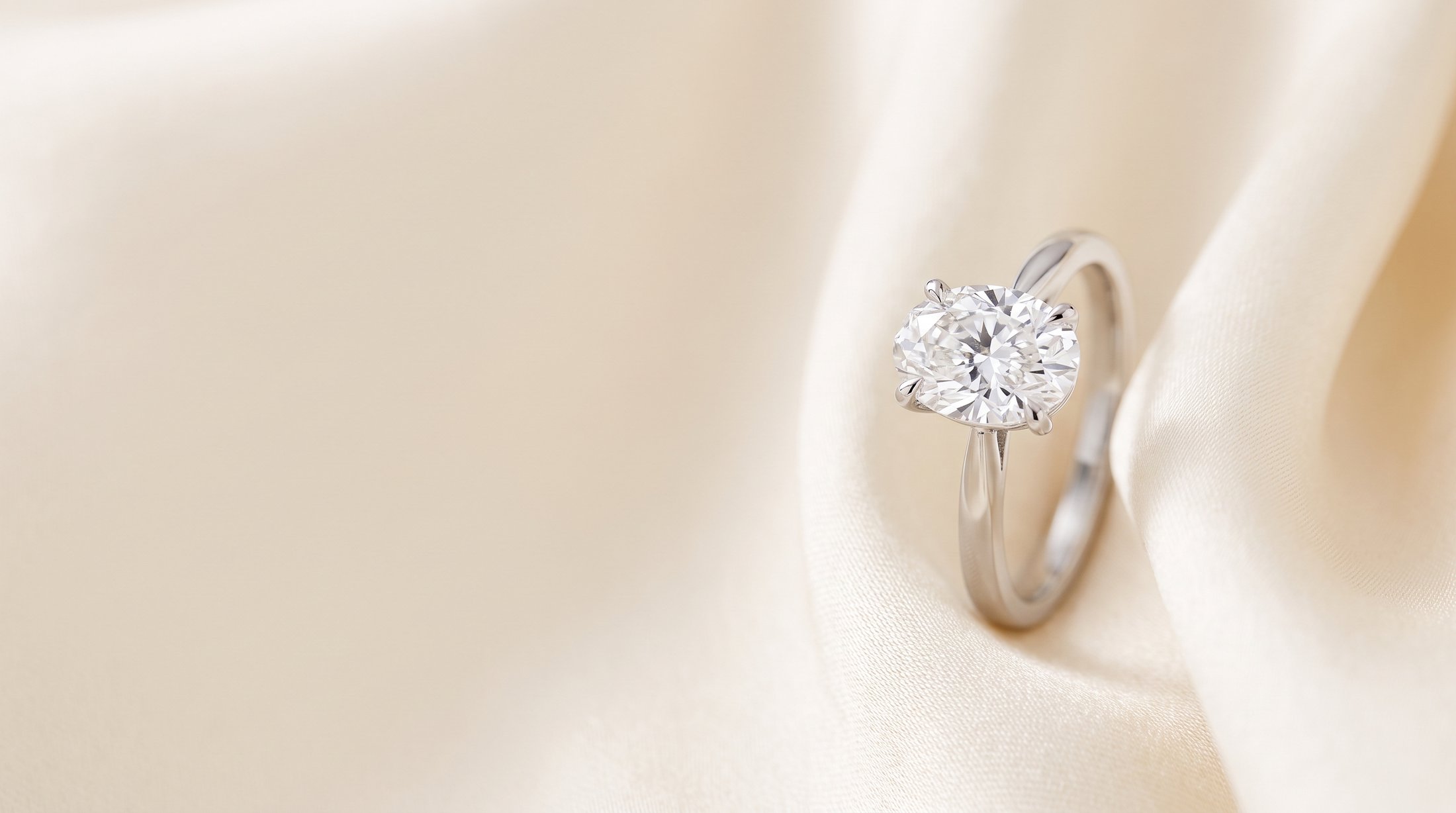 An oval diamond solitaire ring resting on cream silk