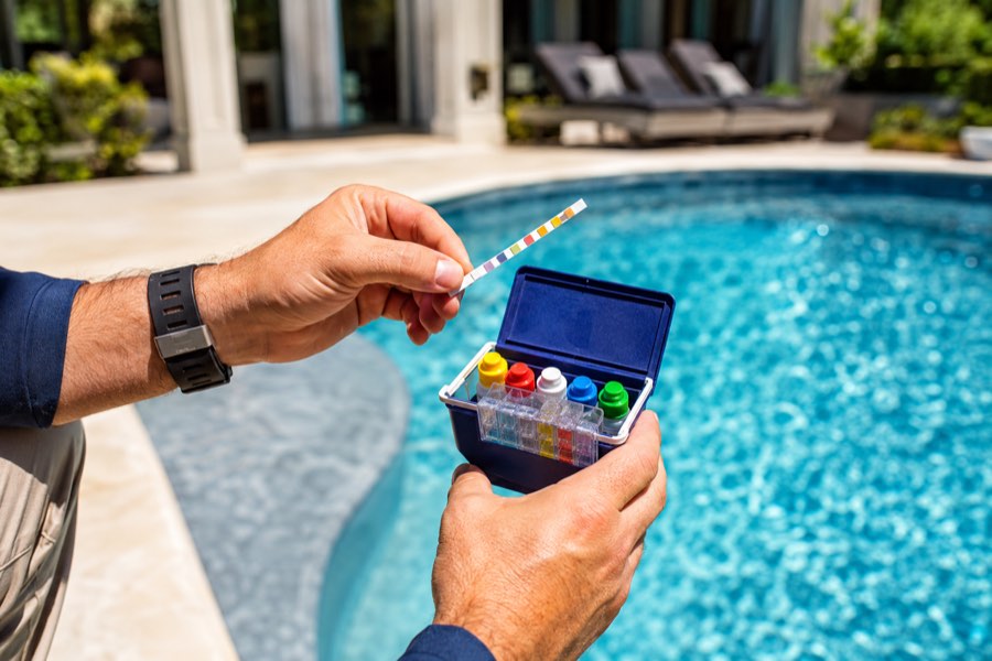 Hands holding a test strip comparator beside pool water
